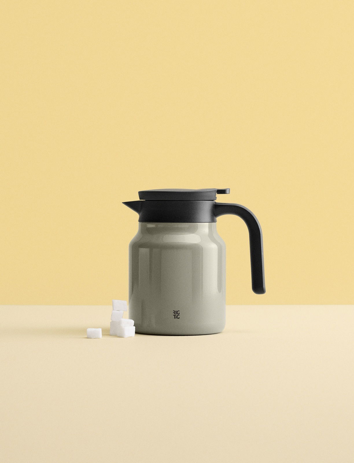 Graue Isolierkanne mit schwarzem Griff und Deckel, seitliche Ansicht, auf hellem Hintergrund mit Zuckerwürfeln.