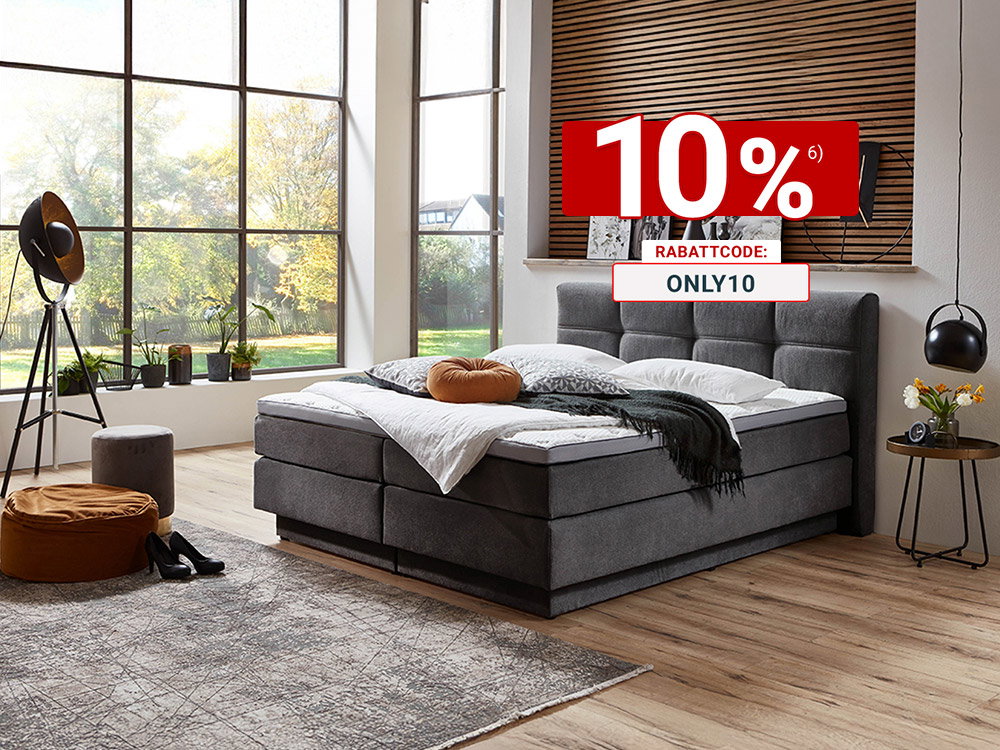 Modern eingerichtetes Schlafzimmer mit grauem Boxspringbett, dekorativer Holzlamellen-Wand, großen Fensterfronten und Blick in den Garten.