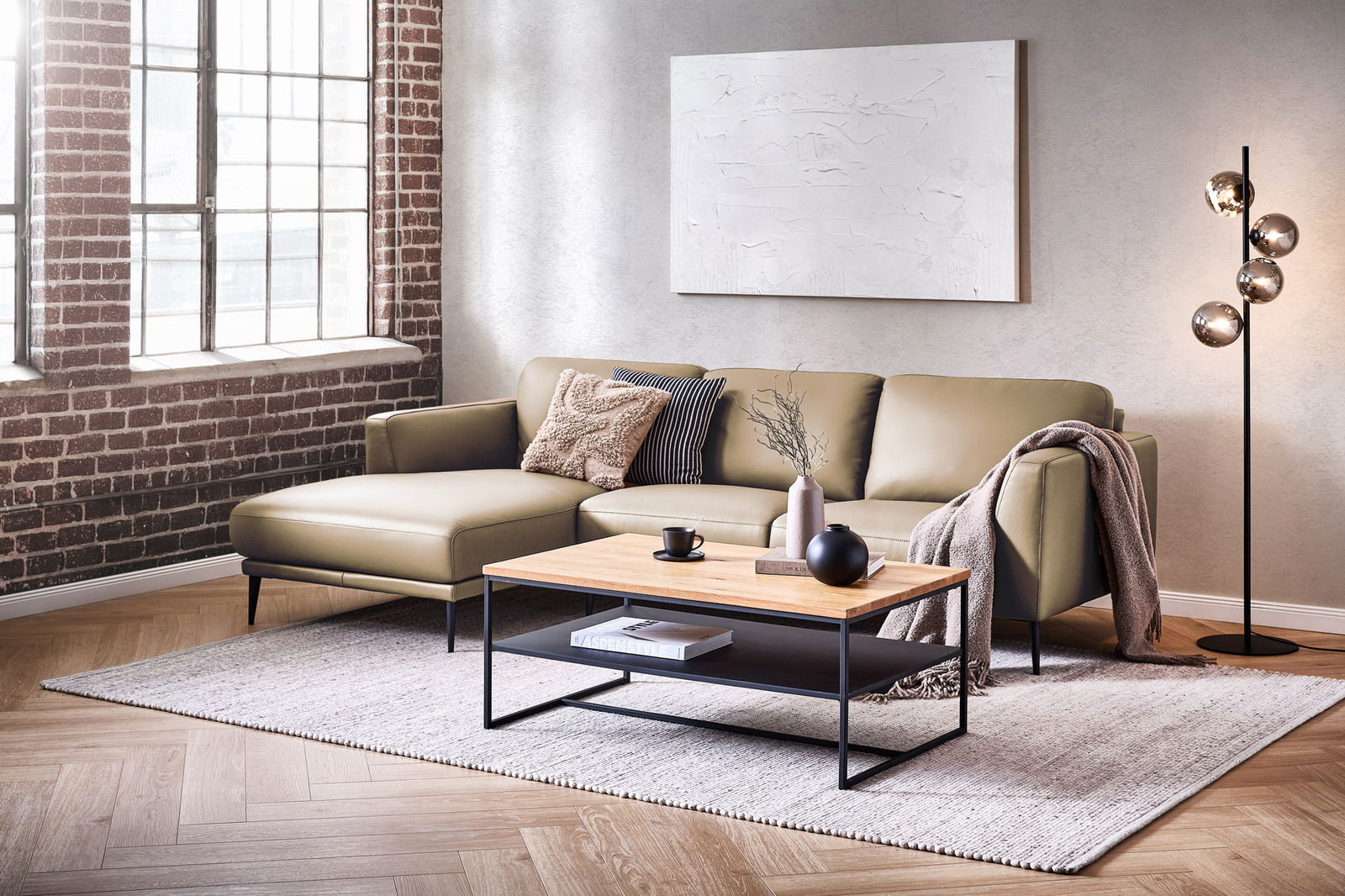 Moderne Longchairkombination in einem stilvollen Wohnzimmer mit Backsteinwand und großen Fenstern, aus seitlicher Perspektive fotografiert.