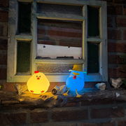 Zwei leuchtende Akku-Nachtlichter in Form von Enten, eine gelb und eine blau, auf einem Fensterbrett aus Holz, frontal betrachtet.