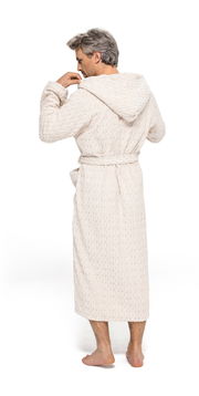 Rückansicht eines Mannes in einem cremefarbenen Kapuzenmantel aus Strickstoff, barfuß stehend.