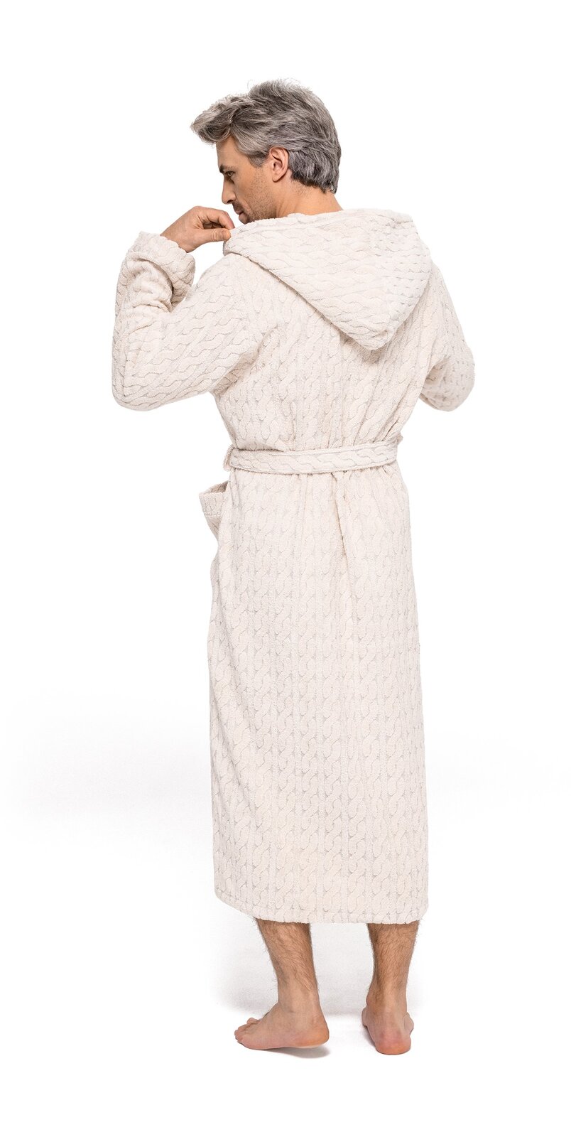 Rückansicht eines Mannes in einem cremefarbenen Kapuzenmantel aus Strickstoff, barfuß stehend.