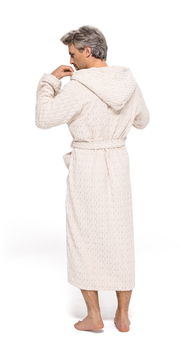 Rückansicht eines Mannes in einem cremefarbenen Kapuzenmantel aus Strickstoff, barfuß stehend.