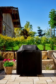 Abdeckhaube für BBQ-Station G4 in einem Garten, frontal fotografiert, mit einem Haus im Hintergrund.