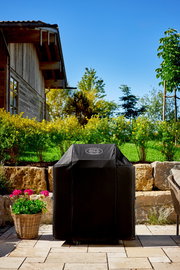 Abdeckhaube für BBQ-Station G4 in einem Garten, frontal fotografiert, mit einem Haus im Hintergrund.
