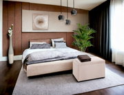 Modernes Schlafzimmer mit großem Polsterbett in Beige, grauer Bettwäsche und gepolsterter Sitzbank am Fußende, drei schwarzen Pendelleuchten, großem Teppich und Pflanze am Fenster; Perspektive: frontale, leicht seitliche Weitwinkelansicht.