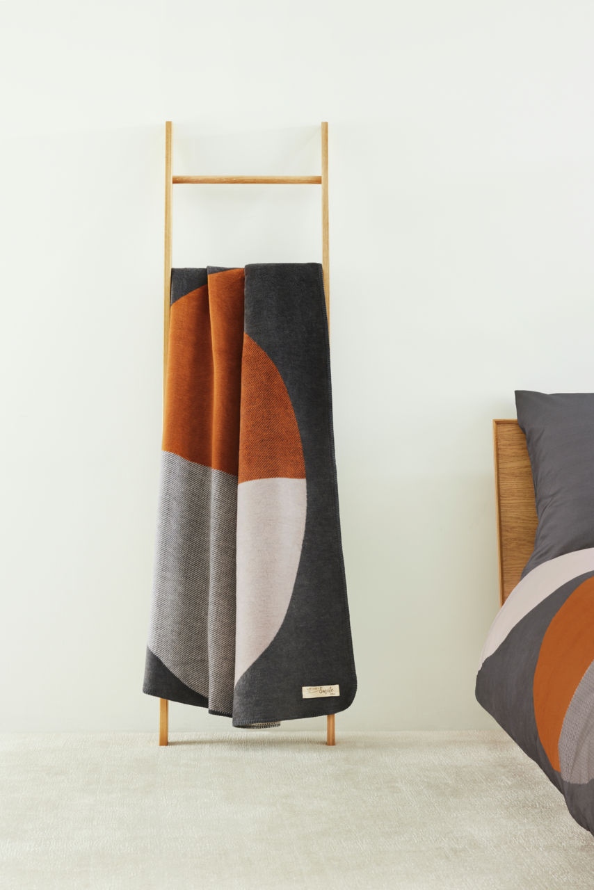 Jacquard Decke in modernen geometrischen Mustern mit warmen Erdtönen, drapiert auf einer Holzleiter, seitliche Perspektive.