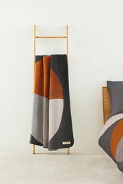 Jacquard Decke in modernen geometrischen Mustern mit warmen Erdtönen, drapiert auf einer Holzleiter, seitliche Perspektive.