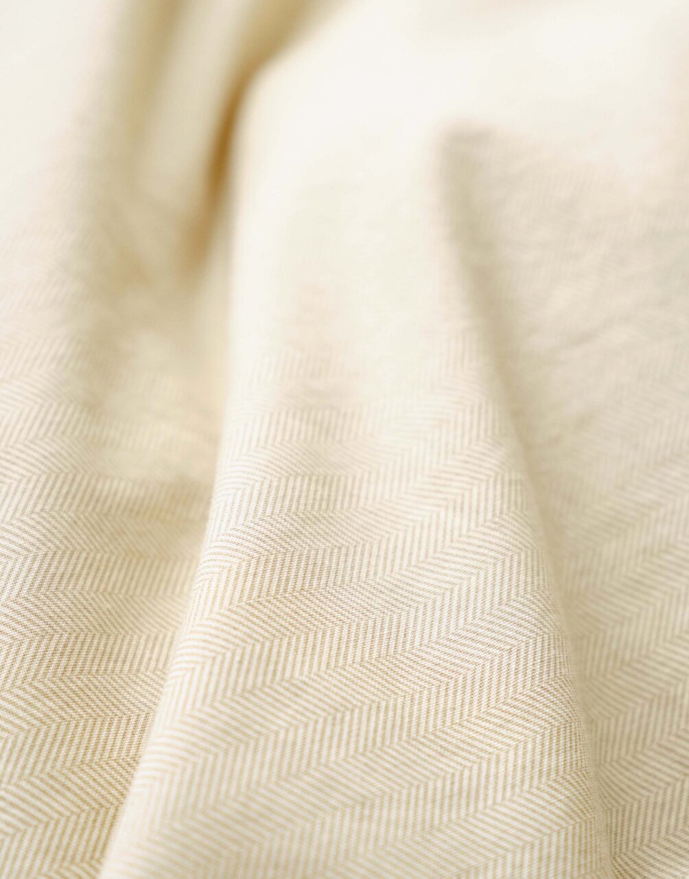 Nahaufnahme einer cremefarbenen Bettwäsche mit dezentem Fischgrätenmuster