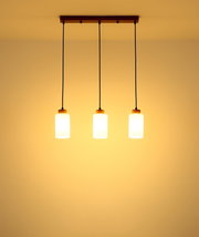 Hanglamp met drie lampen, voorzien van drie cilindervormige, opaalwitte glazen kappen aan een zwarte kabel en een rechthoekige houten kap, van voren en van onderaf tegen het plafond gefotografeerd, warm licht