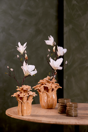 Zwei dekorative Vasen mit weißen Blumen auf einem Holztisch, fotografiert aus einer seitlichen Perspektive.