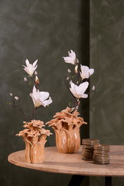 Zwei dekorative Vasen mit weißen Blumen auf einem Holztisch, fotografiert aus einer seitlichen Perspektive.