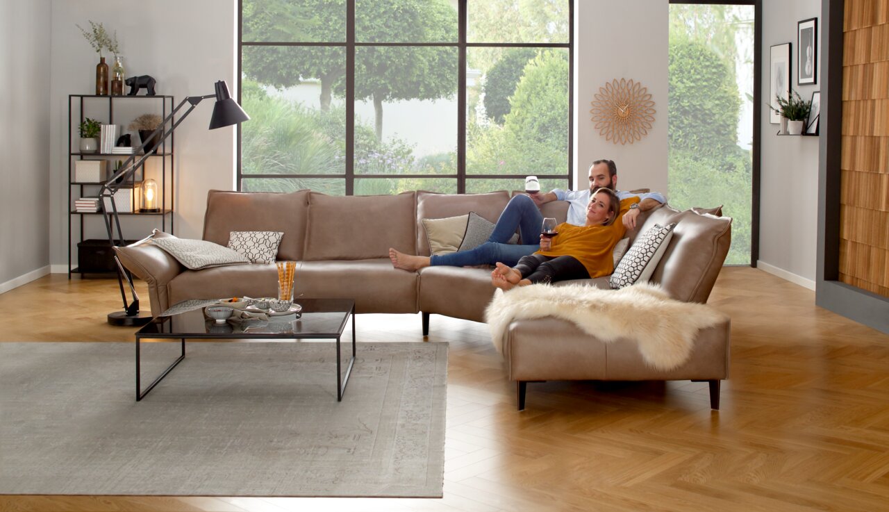 Gemütliche Polsterrundecke in einem modernen Wohnzimmer, seitliche Perspektive, mit einem Paar, das entspannt darauf sitzt.