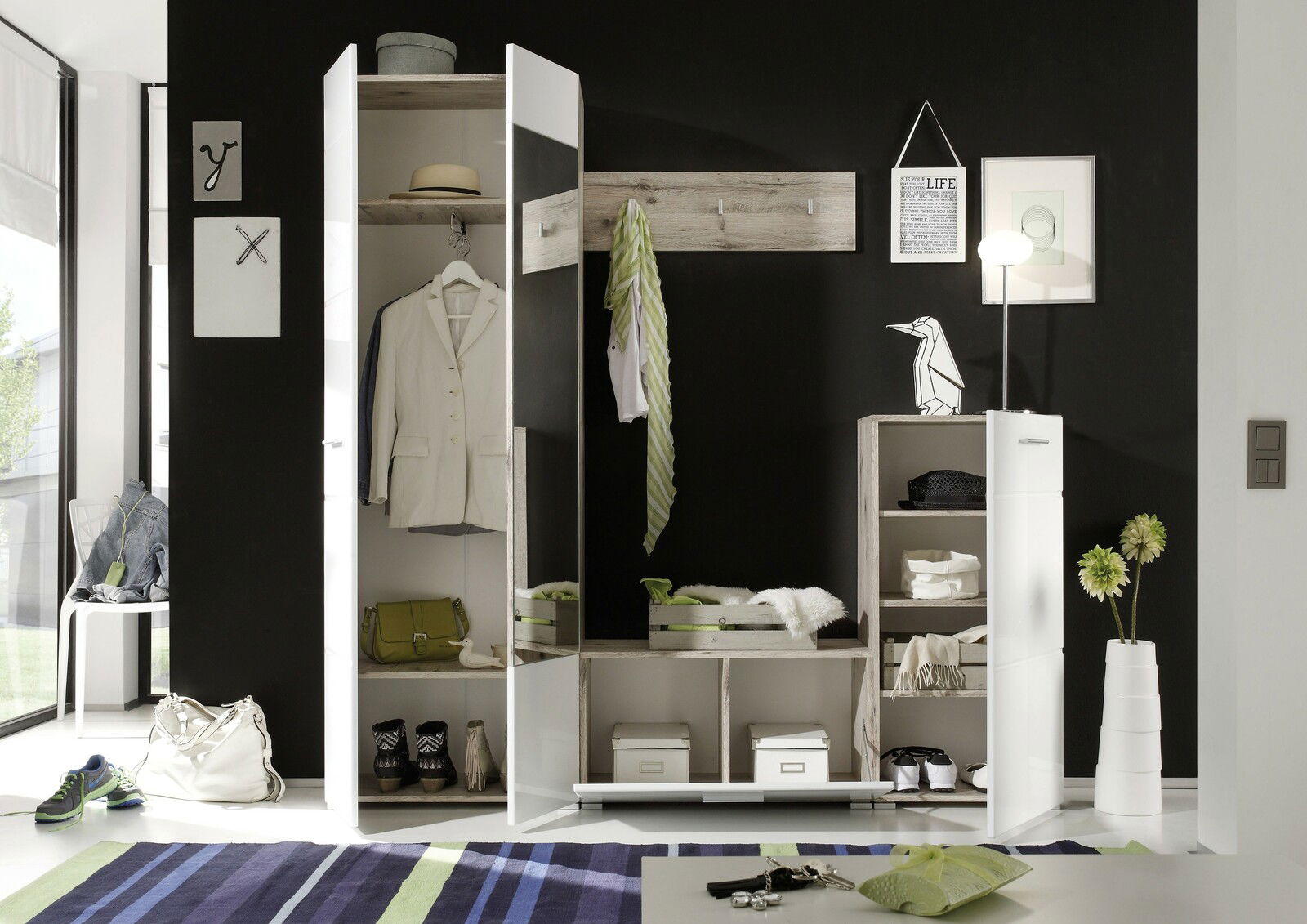 Moderne Garderobenkombination in einem stilvollen Raum mit schwarzer Wand, bestehend aus einem weißen Schrank mit Spiegel, offenen Regalen und Hakenleiste, frontal betrachtet.
