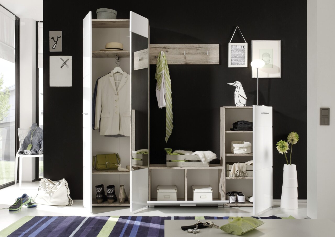 Moderne Garderobenkombination in einem stilvollen Raum mit schwarzer Wand, bestehend aus einem weißen Schrank mit Spiegel, offenen Regalen und Hakenleiste, frontal betrachtet.