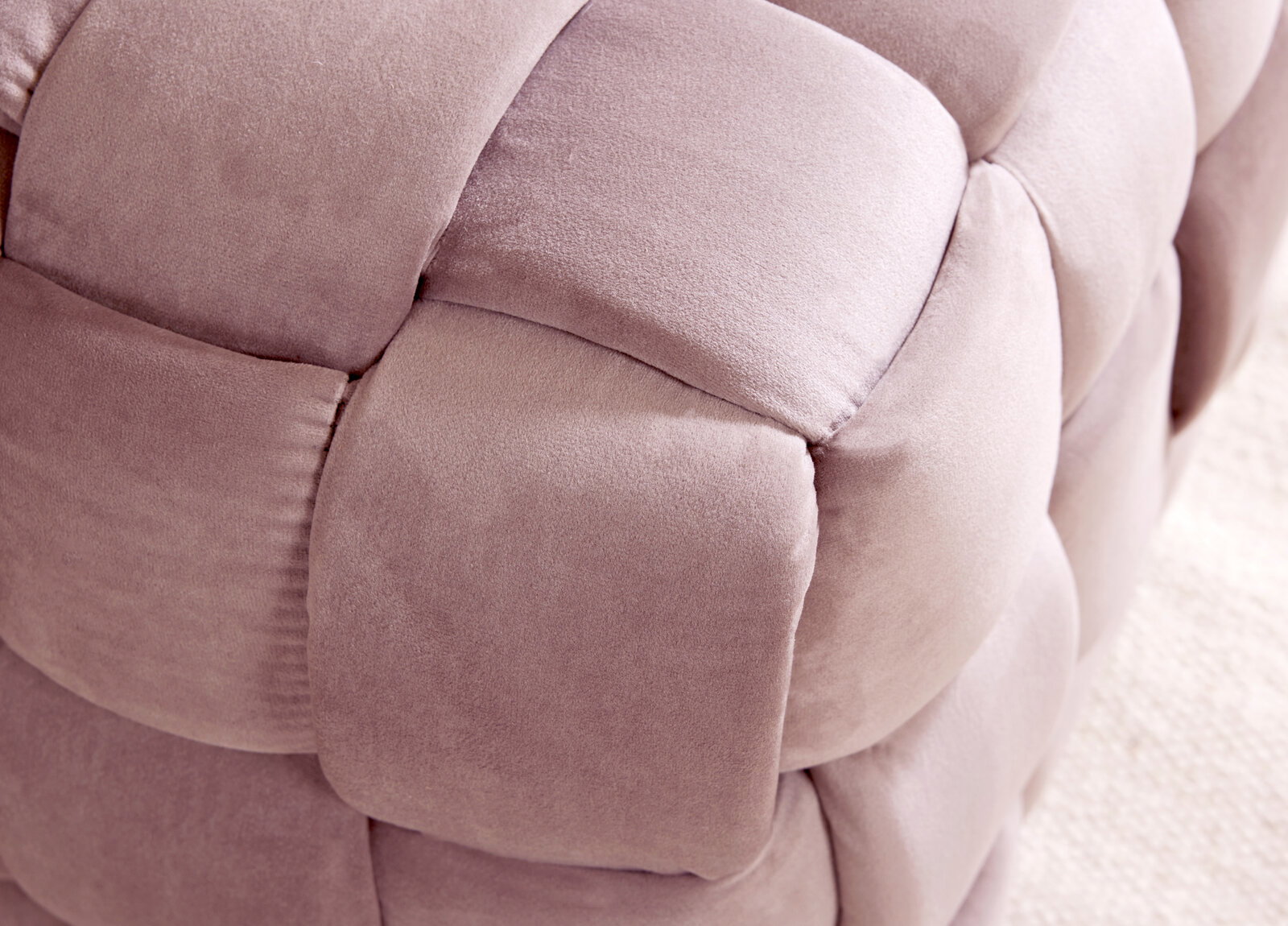 Nahaufnahme eines gepolsterten Hockers mit weichem, rosa Stoff in geflochtener Optik.