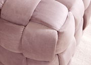 Nahaufnahme eines gepolsterten Hockers mit weichem, rosa Stoff in geflochtener Optik.