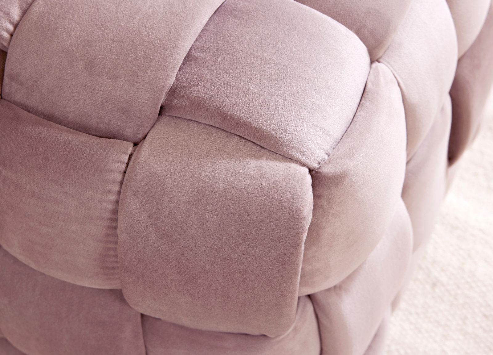 Nahaufnahme eines gepolsterten Hockers mit weichem, rosa Stoff in geflochtener Optik.