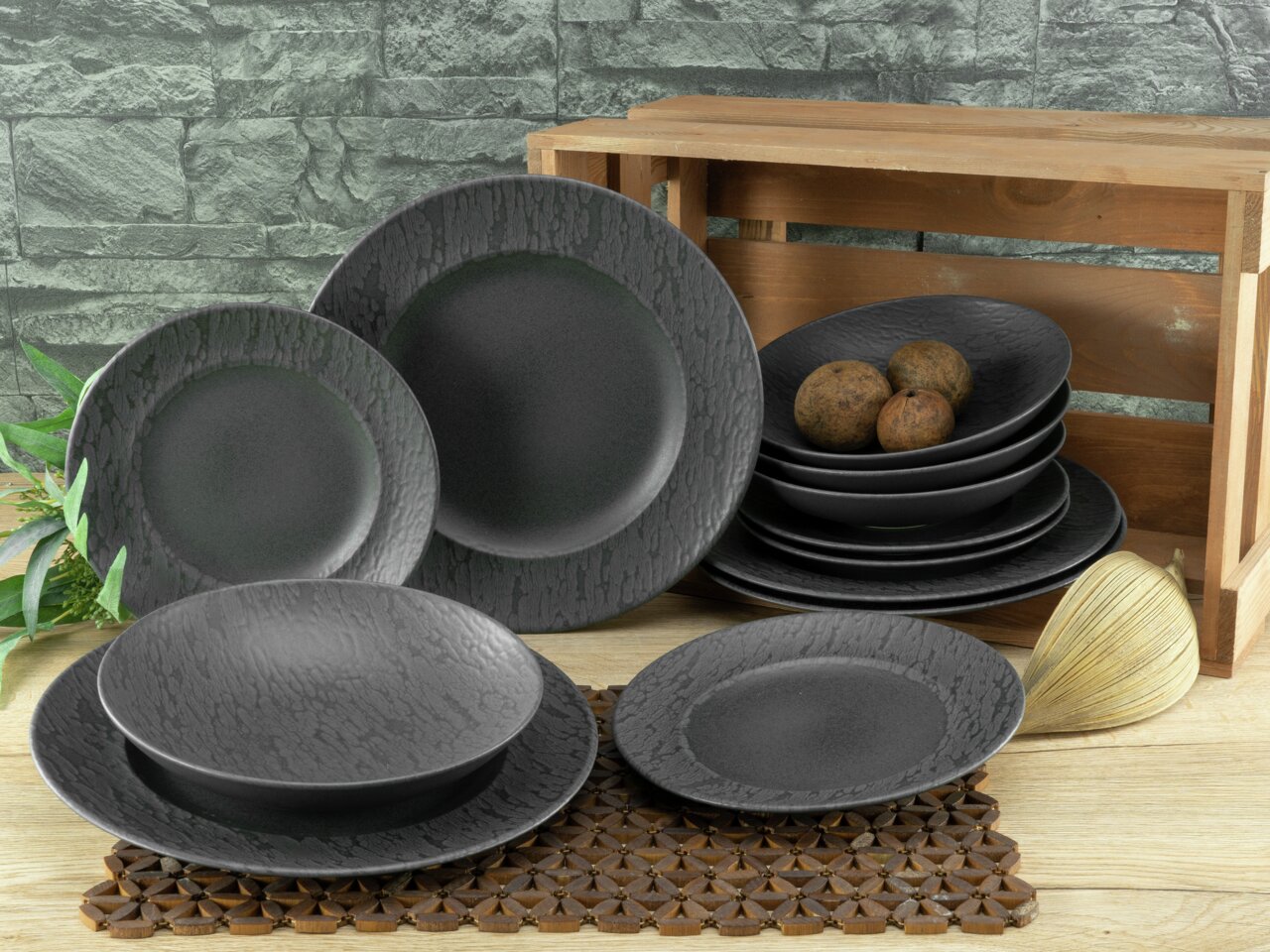 Schieferfarbenes 12-teiliges Tellerset in moderner, rustikaler Optik, präsentiert auf einem Holztisch mit dekorativen Elementen, seitliche Perspektive.