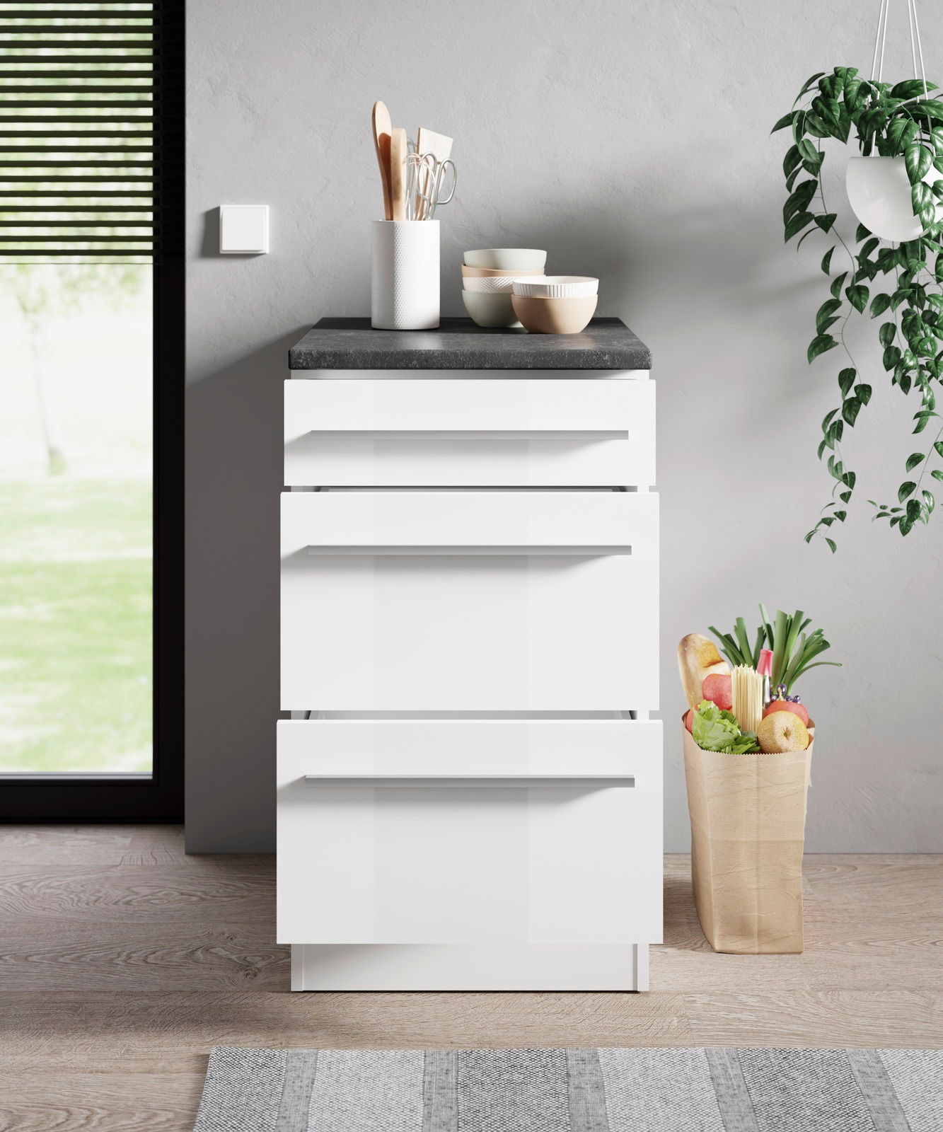 Moderner weißer Unterschrank mit vier Schubladen, von vorne betrachtet, dekoriert mit Küchenutensilien und Schalen auf der Arbeitsplatte, neben einer Papiertüte mit frischen Lebensmitteln.