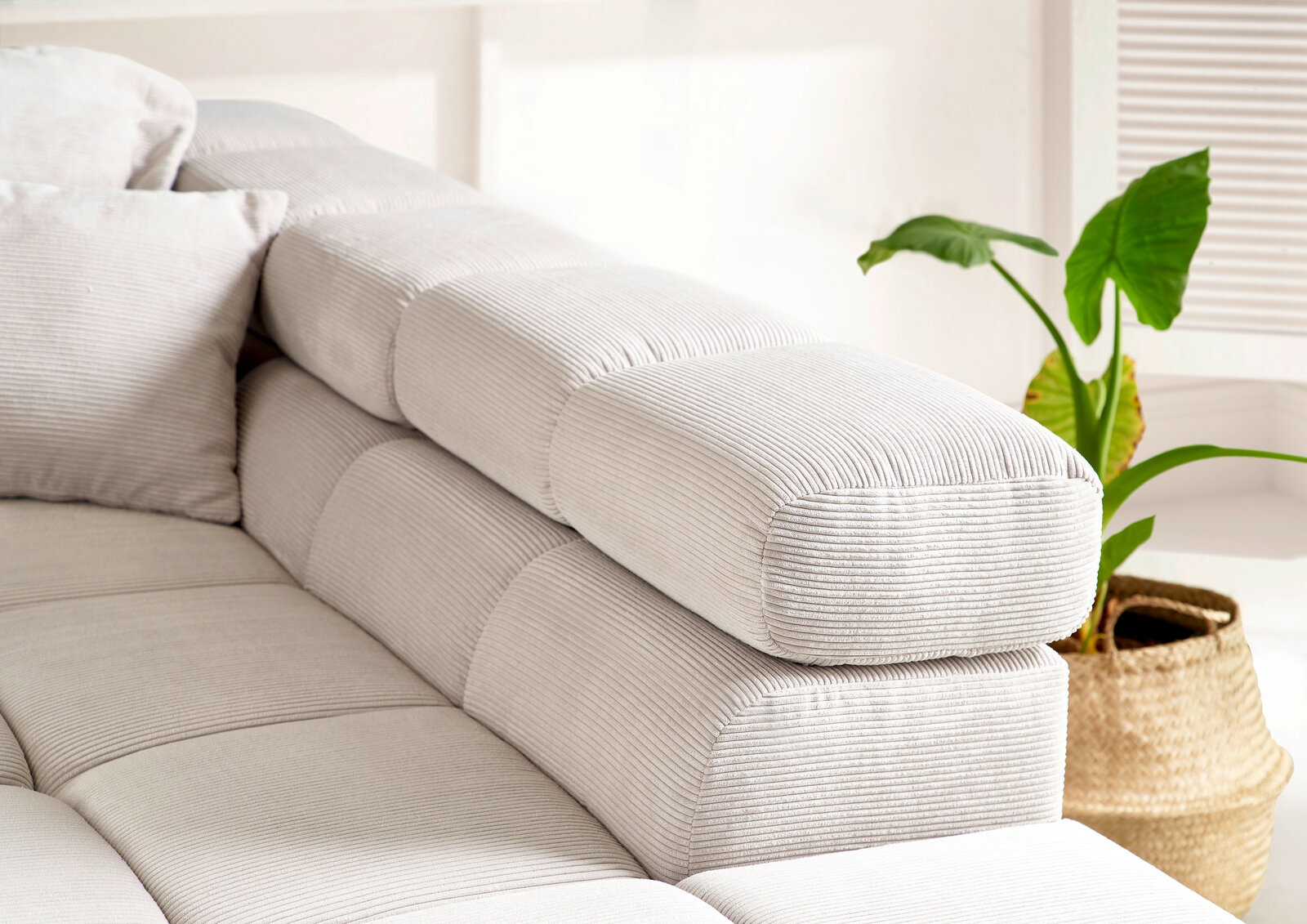 Nahaufnahme einer modernen, hellgrauen Rundecke mit geripptem Stoffbezug und Kissen, seitliche Perspektive.