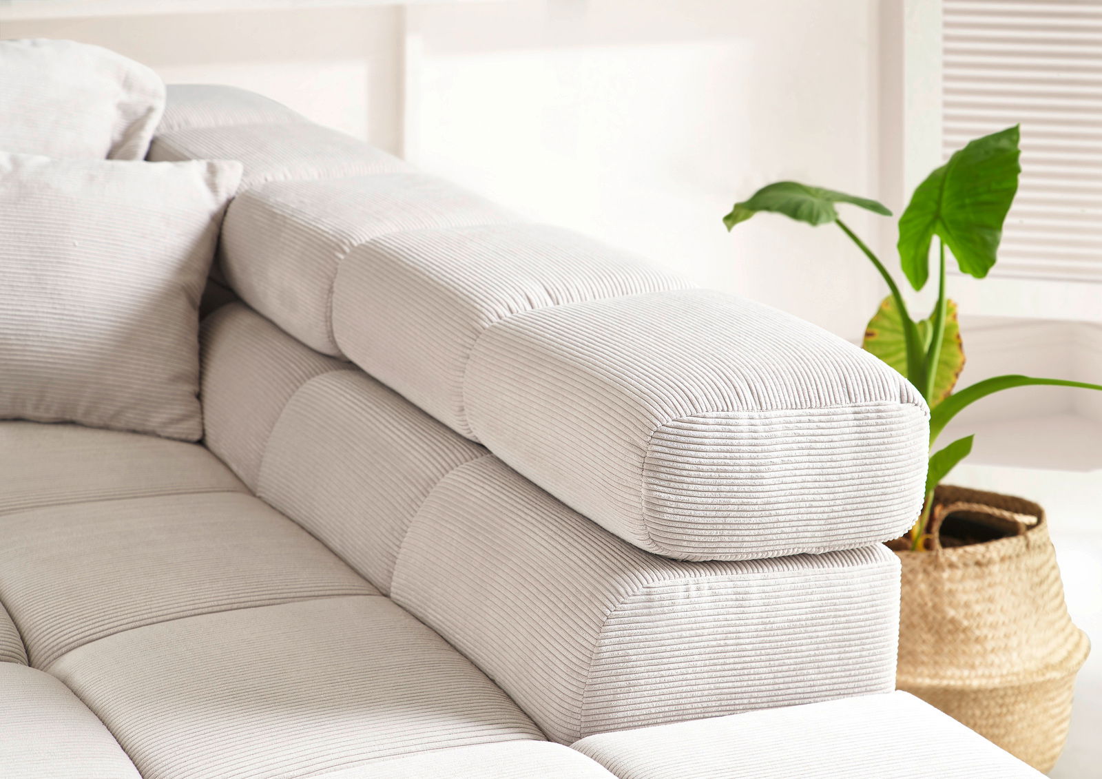 Nahaufnahme einer modernen, hellgrauen Rundecke mit geripptem Stoffbezug und Kissen, seitliche Perspektive.