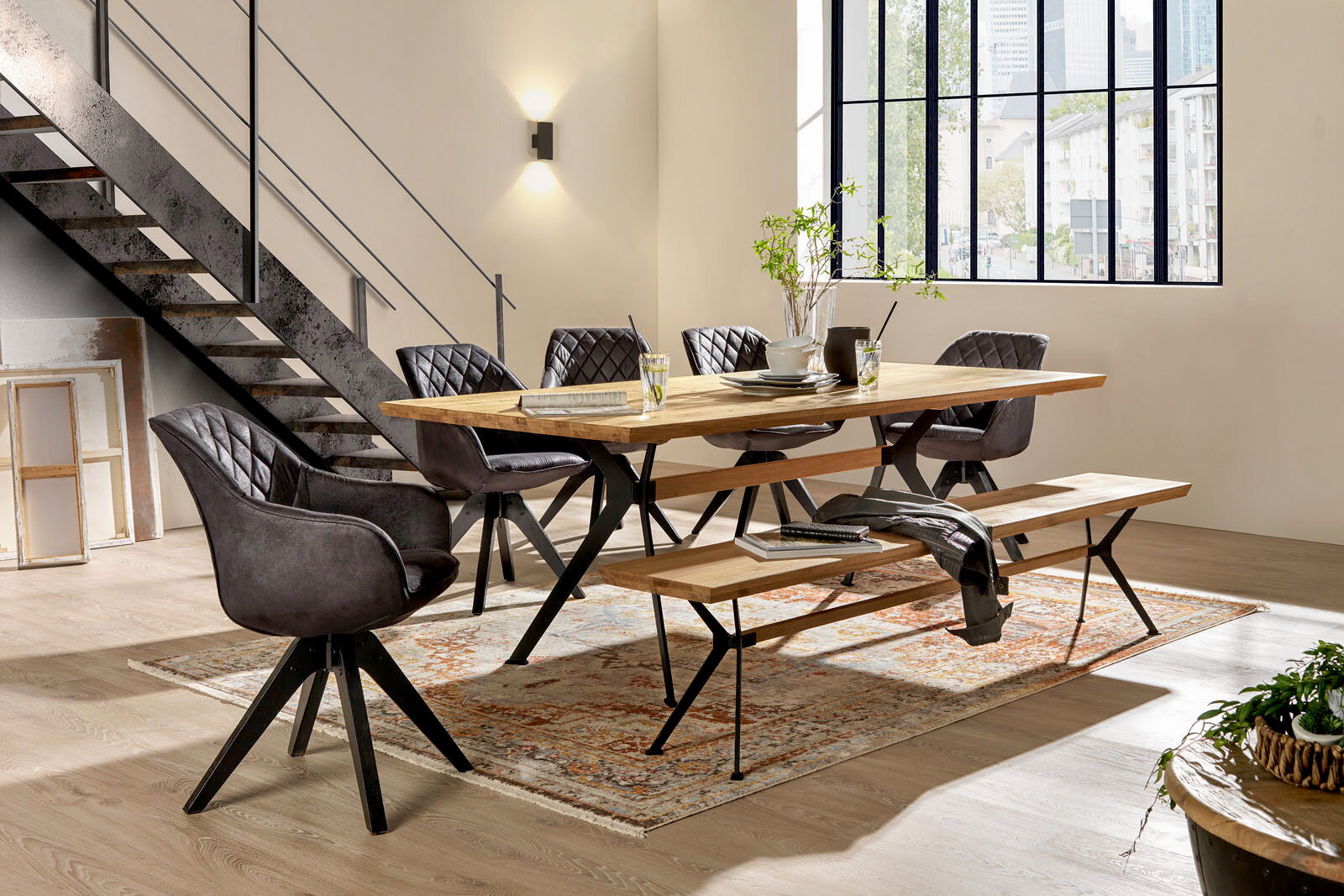 Esszimmer mit modernem Esstisch aus Holz und Metall, umgeben von gepolsterten Stühlen und einer Sitzbank, seitliche Perspektive.