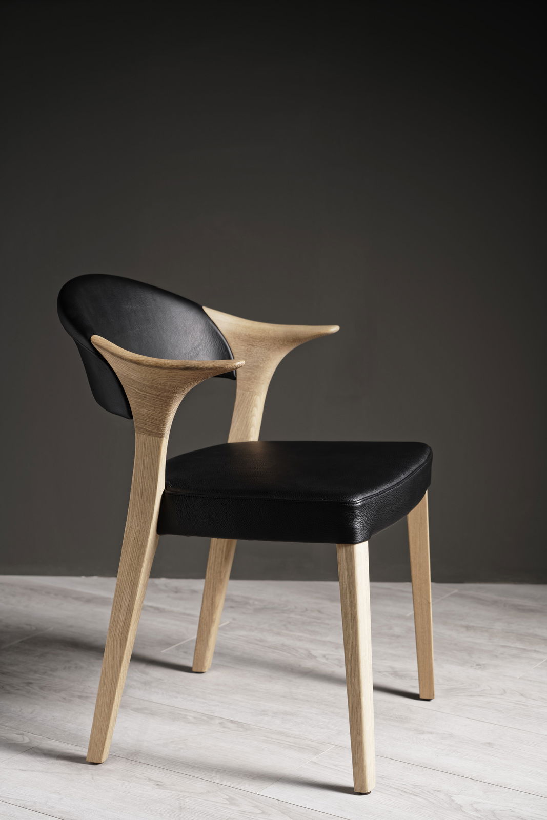 Moderner Armlehnstuhl aus Holz mit schwarzem Lederbezug, seitliche Perspektive