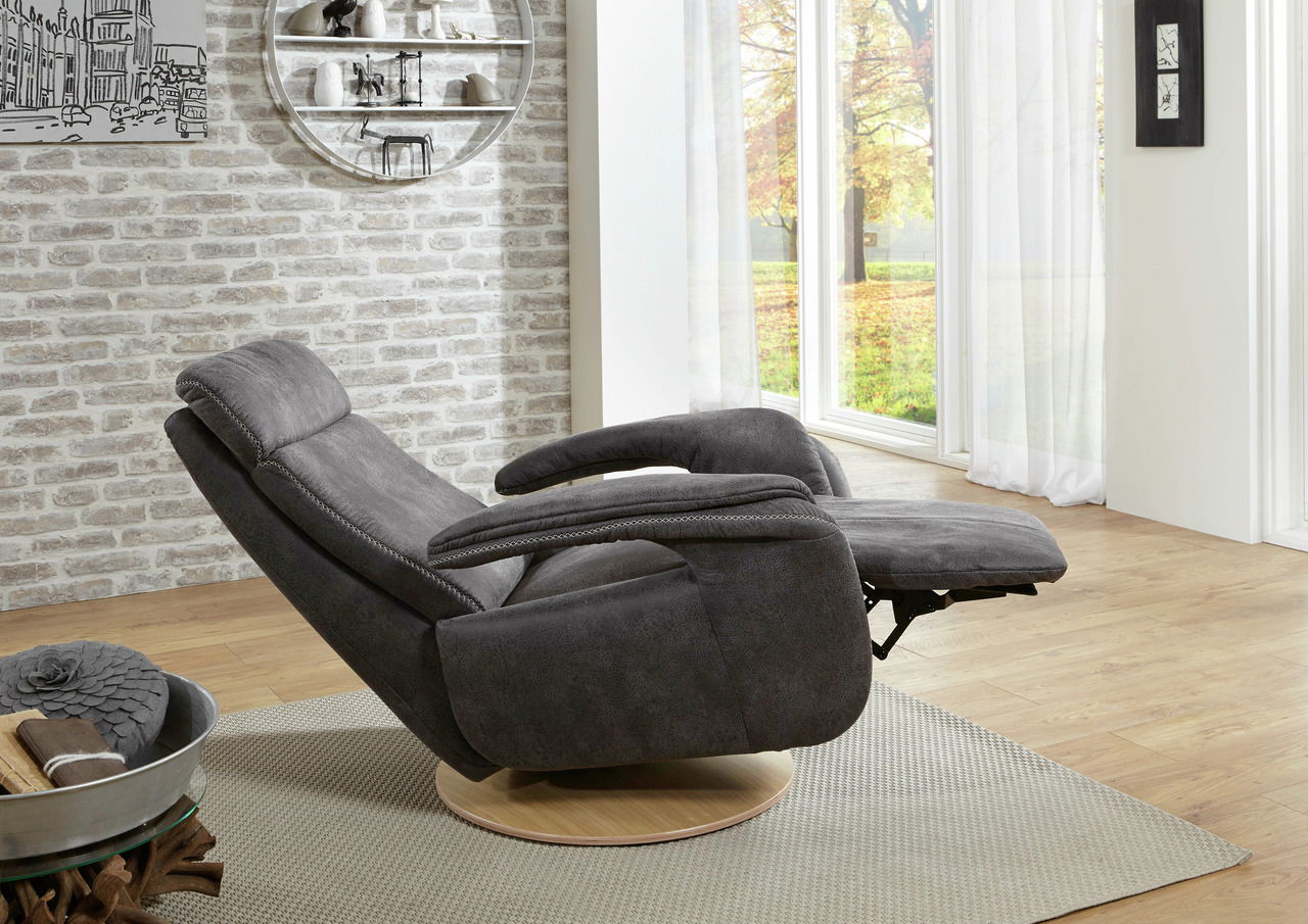 Grauer Relaxsessel in Liegeposition, seitliche Perspektive, vor einer Backsteinwand und großen Fenstern mit Blick auf einen herbstlichen Garten.