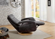 Grijze relaxfauteuil in ligstand, gezien vanaf de zijkant, voor een bakstenen muur en grote ramen met uitzicht op een herfsttuin.