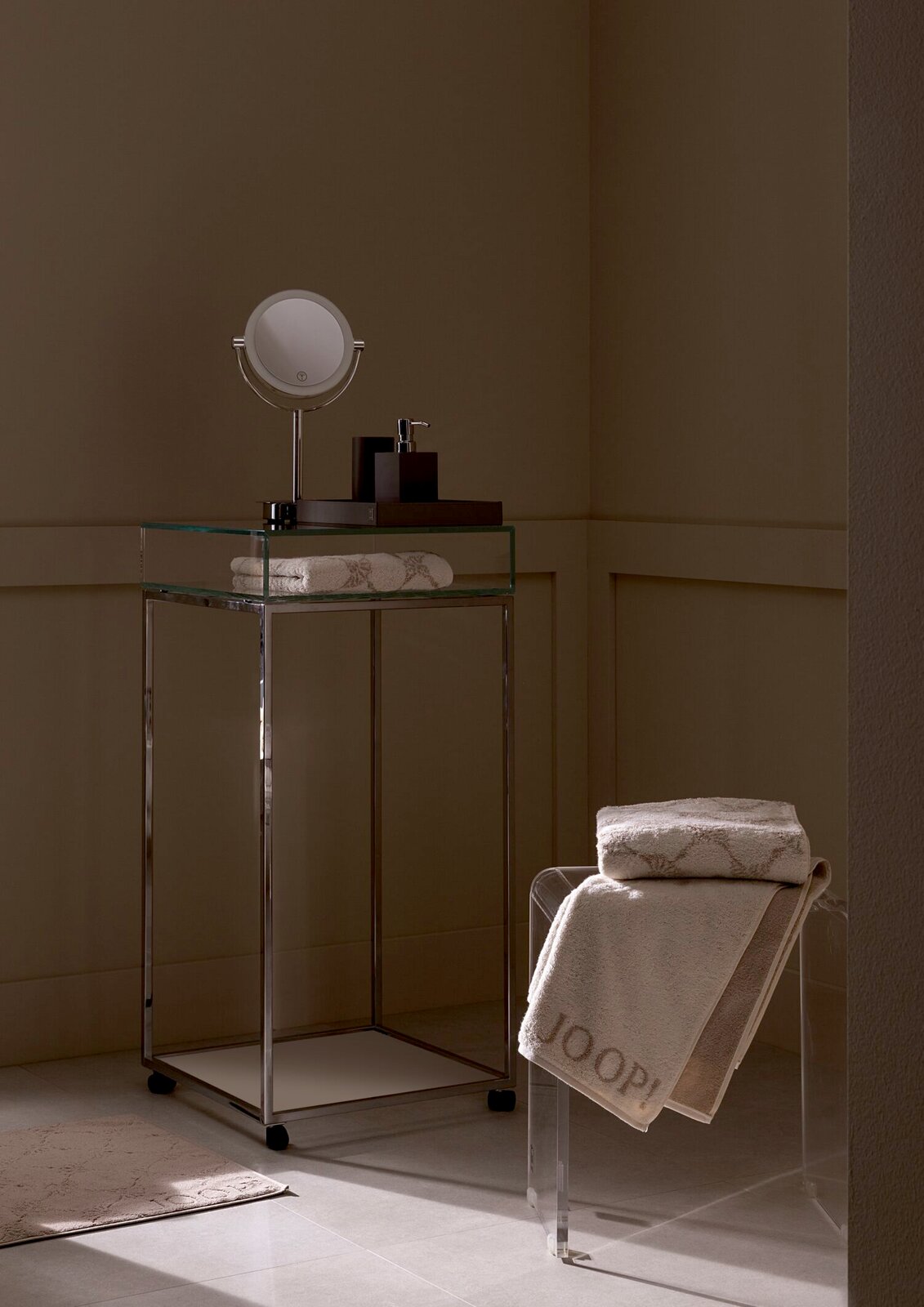 Luxuriöses Gästetuch in einem stilvollen Badezimmer, auf einem transparenten Stuhl drapiert, mit einem modernen Waschtisch im Hintergrund. Perspektive von der Seite.