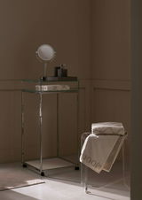 Luxuriöses Gästetuch in einem stilvollen Badezimmer, auf einem transparenten Stuhl drapiert, mit einem modernen Waschtisch im Hintergrund. Perspektive von der Seite.