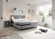 Modernes Boxspringbett in einem hellen Schlafzimmer, seitliche Perspektive, mit grauem Kopfteil und verstellbaren Matratzen, umgeben von stilvoller Dekoration.