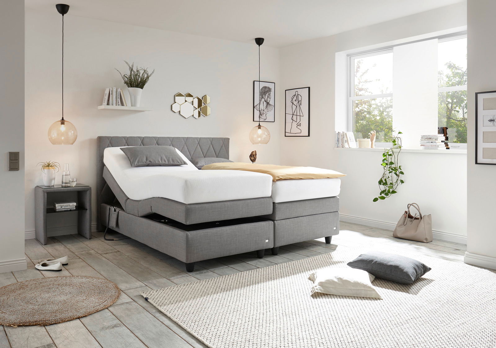 Modernes Boxspringbett in einem hellen Schlafzimmer, seitliche Perspektive, mit grauem Kopfteil und verstellbaren Matratzen, umgeben von stilvoller Dekoration.