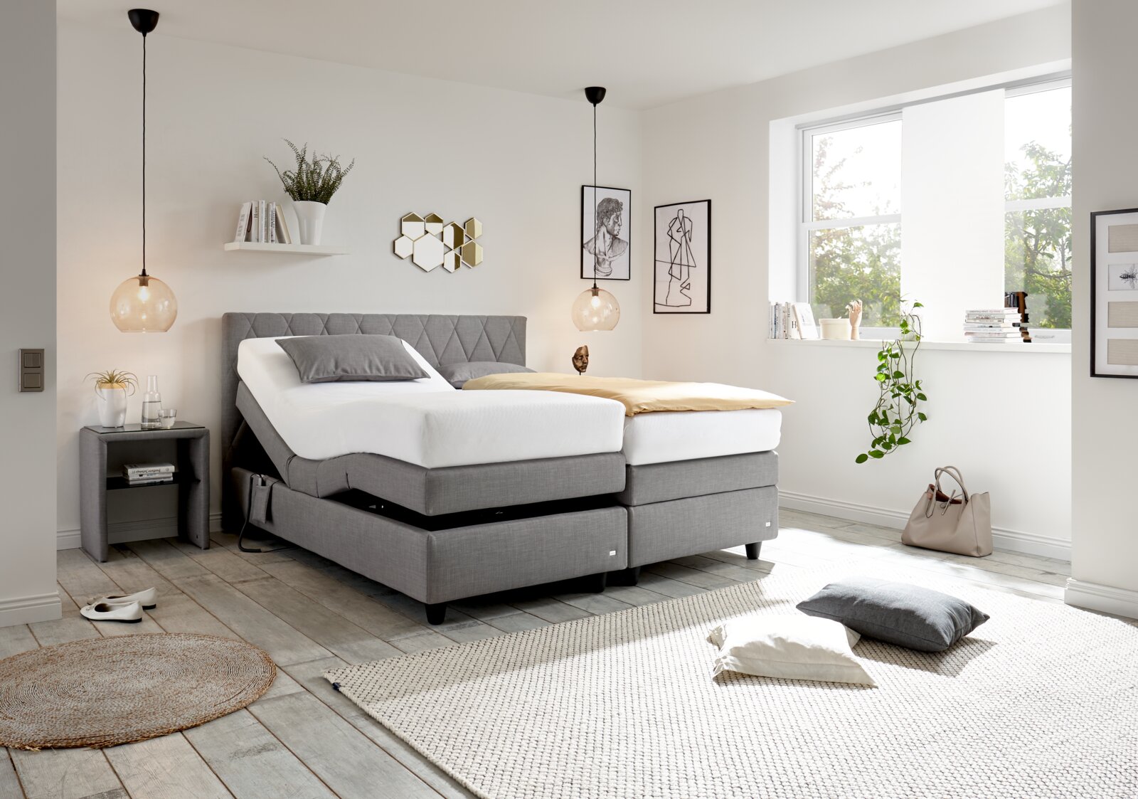 Modernes Boxspringbett in einem hellen Schlafzimmer, seitliche Perspektive, mit grauem Kopfteil und verstellbaren Matratzen, umgeben von stilvoller Dekoration.