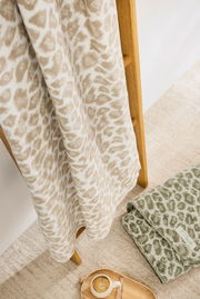 Leopardengemusterte Wohndecke in Beige auf Holzleiter, daneben eine grüne Decke und ein Tablett mit Kaffee, aus der Vogelperspektive.