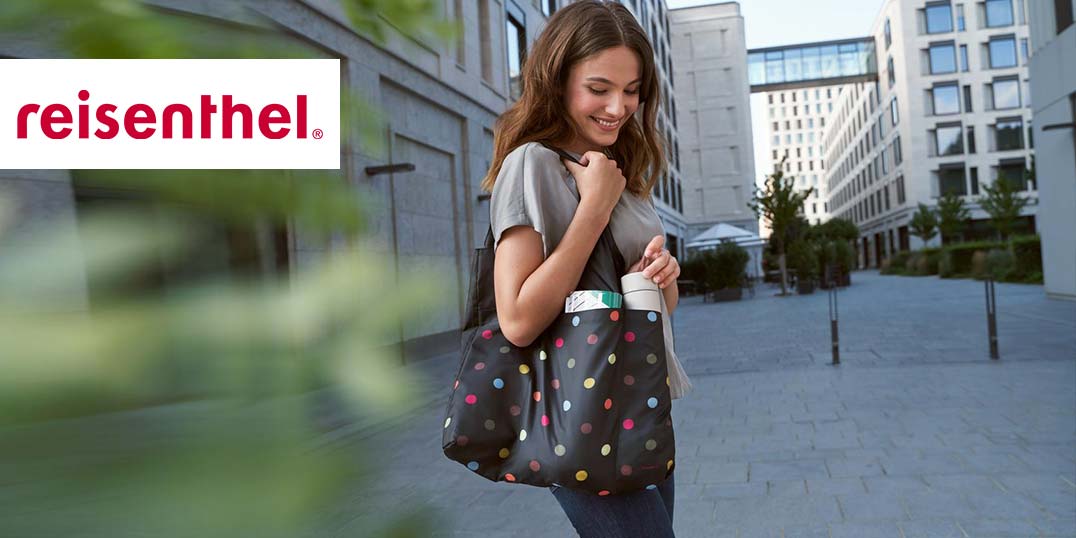 Eine lächelnde Frau mit einer bunten Tasche geht durch eine moderne Stadtstraße..