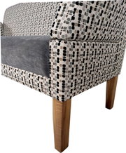Detailansicht schräg von vorne auf einen gepolsterten Sessel mit gemustertem Stoffbezug in Grau/Beige/Schwarz, grauem Sitzkissen und Holzbeinen