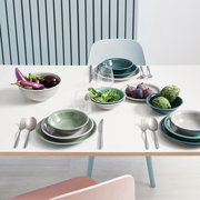 Ein stilvoll gedeckter Tisch mit einem Suppenteller in Nachtblau, umgeben von weiteren Geschirrteilen und frischem Gemüse. Perspektive von oben.