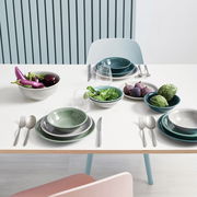 Ein stilvoll gedeckter Tisch mit einem Suppenteller in Nachtblau, umgeben von weiteren Geschirrteilen und frischem Gemüse. Perspektive von oben.