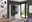 Moderne Garderobenkombination in einem hellen Raum mit großen Fenstern, die einen Blick auf den Garten bieten. Die Garderobe hat eine glänzende weiße Oberfläche mit einem Spiegel und bietet Platz zum Aufhängen von Kleidung. Perspektive von vorne.