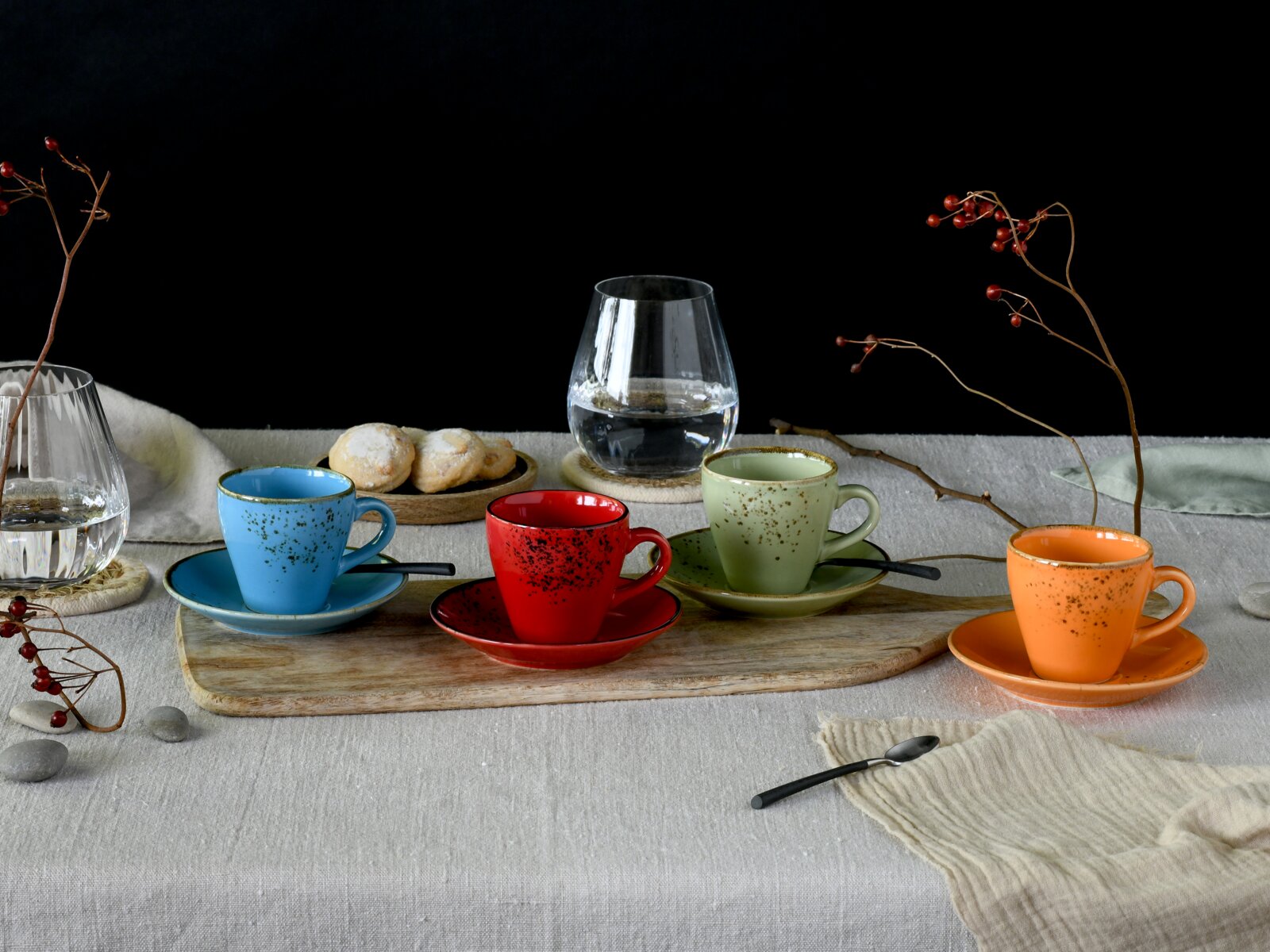 Creatable Espressotassen 8-tlg NATURE COLLECTION Vier bunte Espresso-/Kaffeetassen mit Untertassen (blau, rot, grün, orange) auf Holztablett auf gedecktem Tisch, mit Gläsern und Gebäck im Hintergrund; Perspektive: leicht erhöhte Frontansicht.