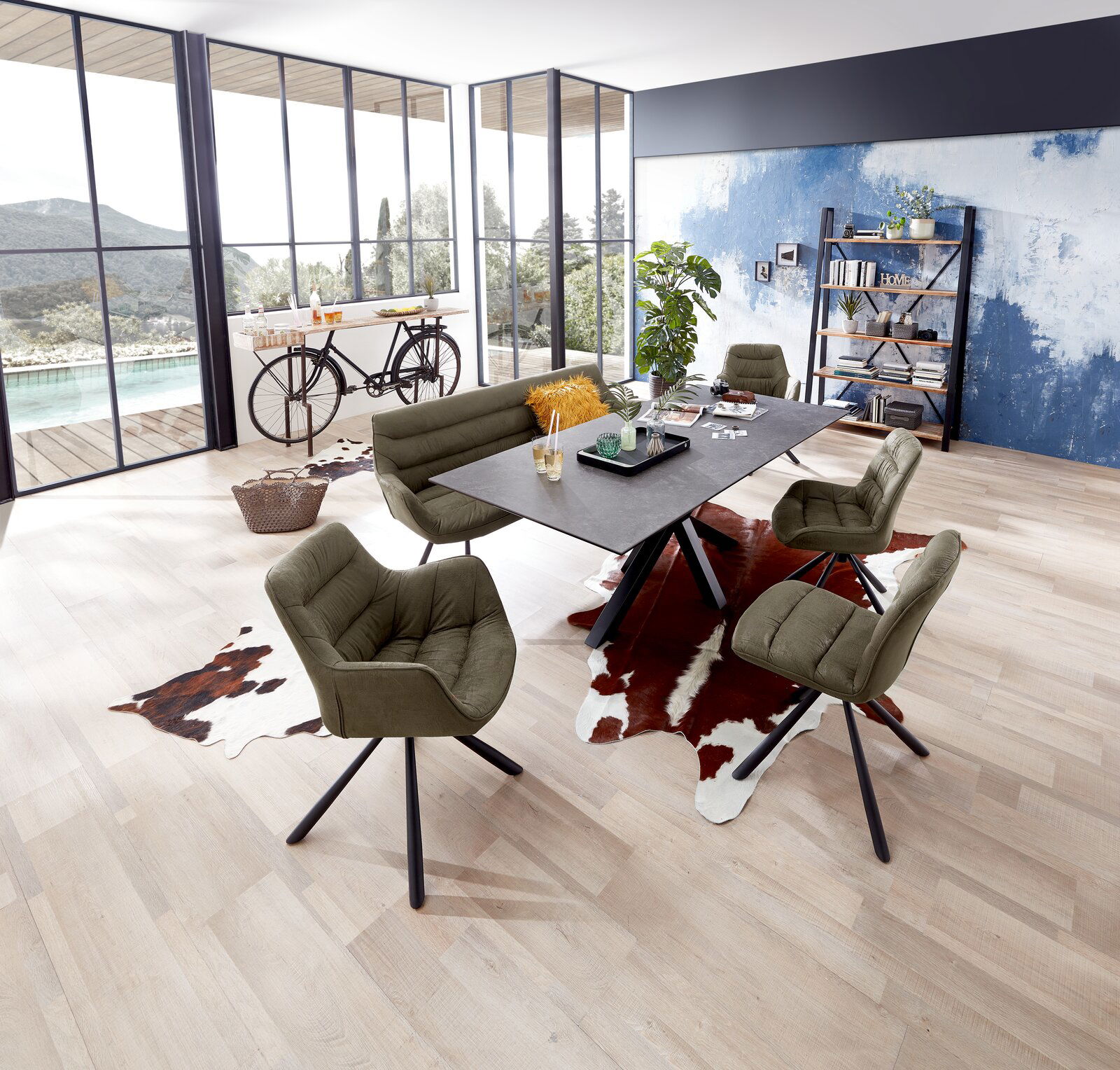 Z2 Esstisch GERD Moderner Esstisch mit dunkler Tischplatte und schwarzen Beinen, umgeben von grünen Polsterstühlen in einem hellen Raum mit großen Fenstern und Holzboden, aus der Vogelperspektive.