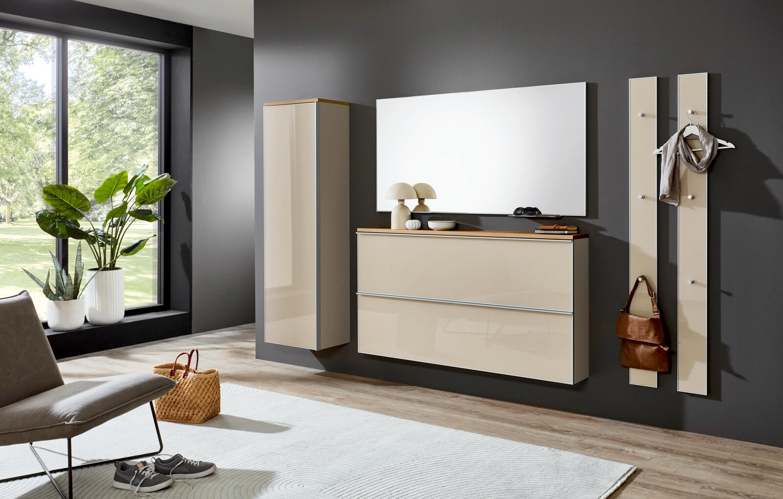 Modernes Wandgarderoben-Set in Beige Hochglanz mit Hängeschrank, Schuhschrank/Kommode, Spiegel und zwei Garderobenpaneelen an dunkelgrauer Wand, frontal aus leicht seitlicher Perspektive aufgenommen.