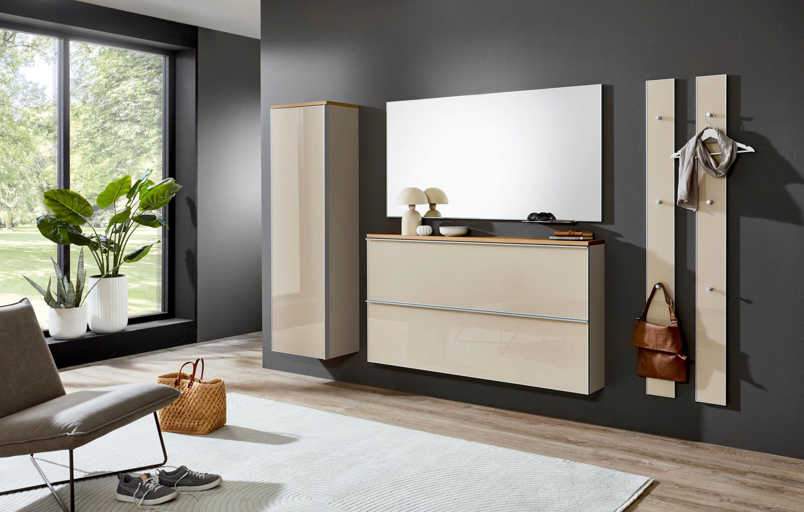 Modernes Wandgarderoben-Set in Beige Hochglanz mit Hängeschrank, Schuhschrank/Kommode, Spiegel und zwei Garderobenpaneelen an dunkelgrauer Wand, frontal aus leicht seitlicher Perspektive aufgenommen.