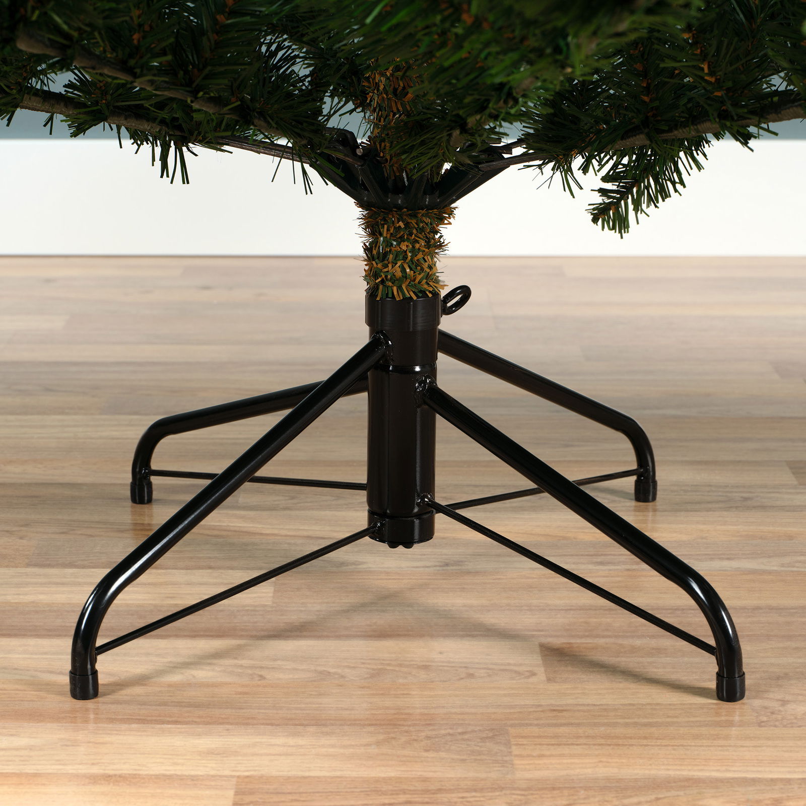 Nahaufnahme des unteren Teils eines künstlichen Weihnachtsbaums mit stabilem Metallständer auf Holzfußboden.