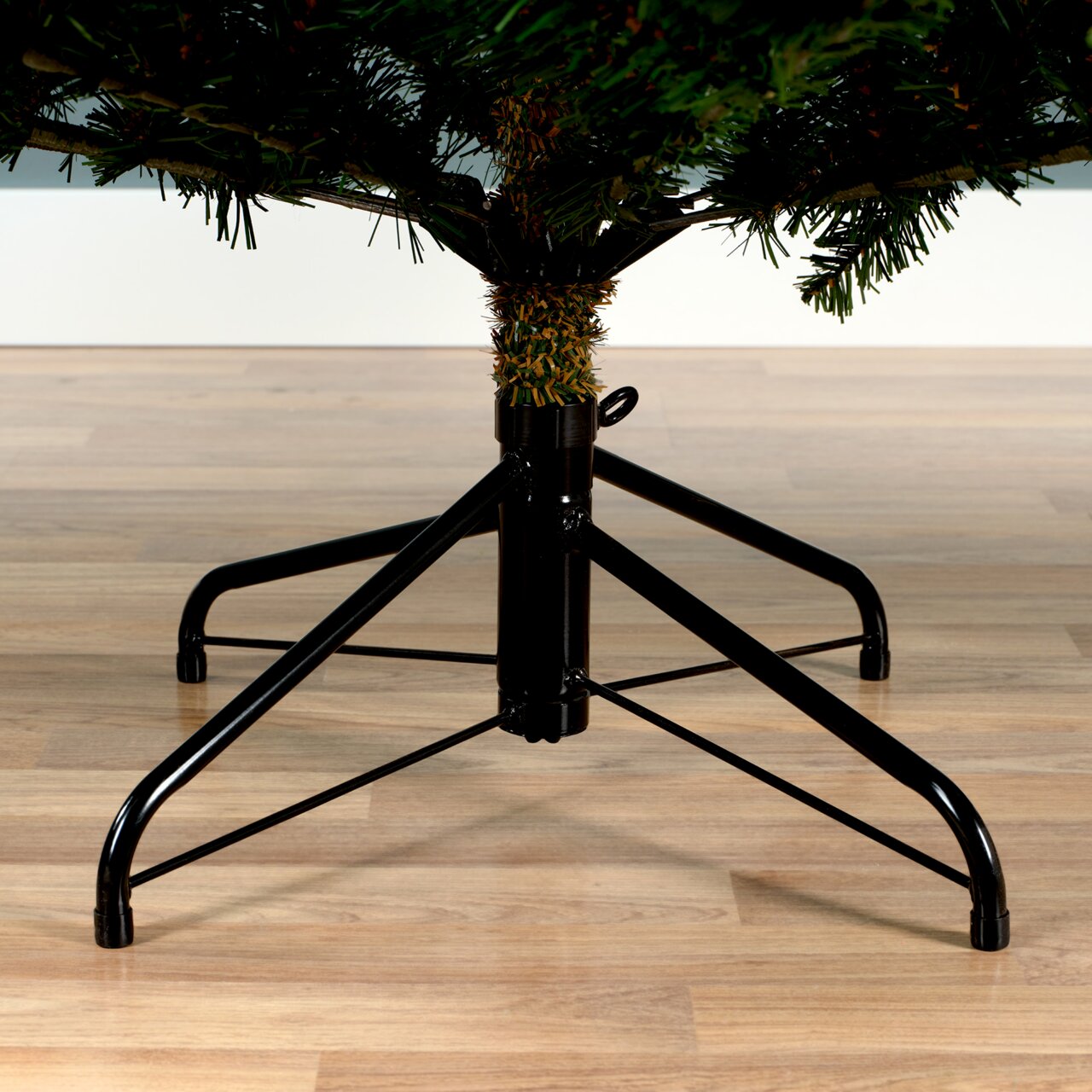 Nahaufnahme des unteren Teils eines künstlichen Weihnachtsbaums mit stabilem Metallständer auf Holzfußboden.