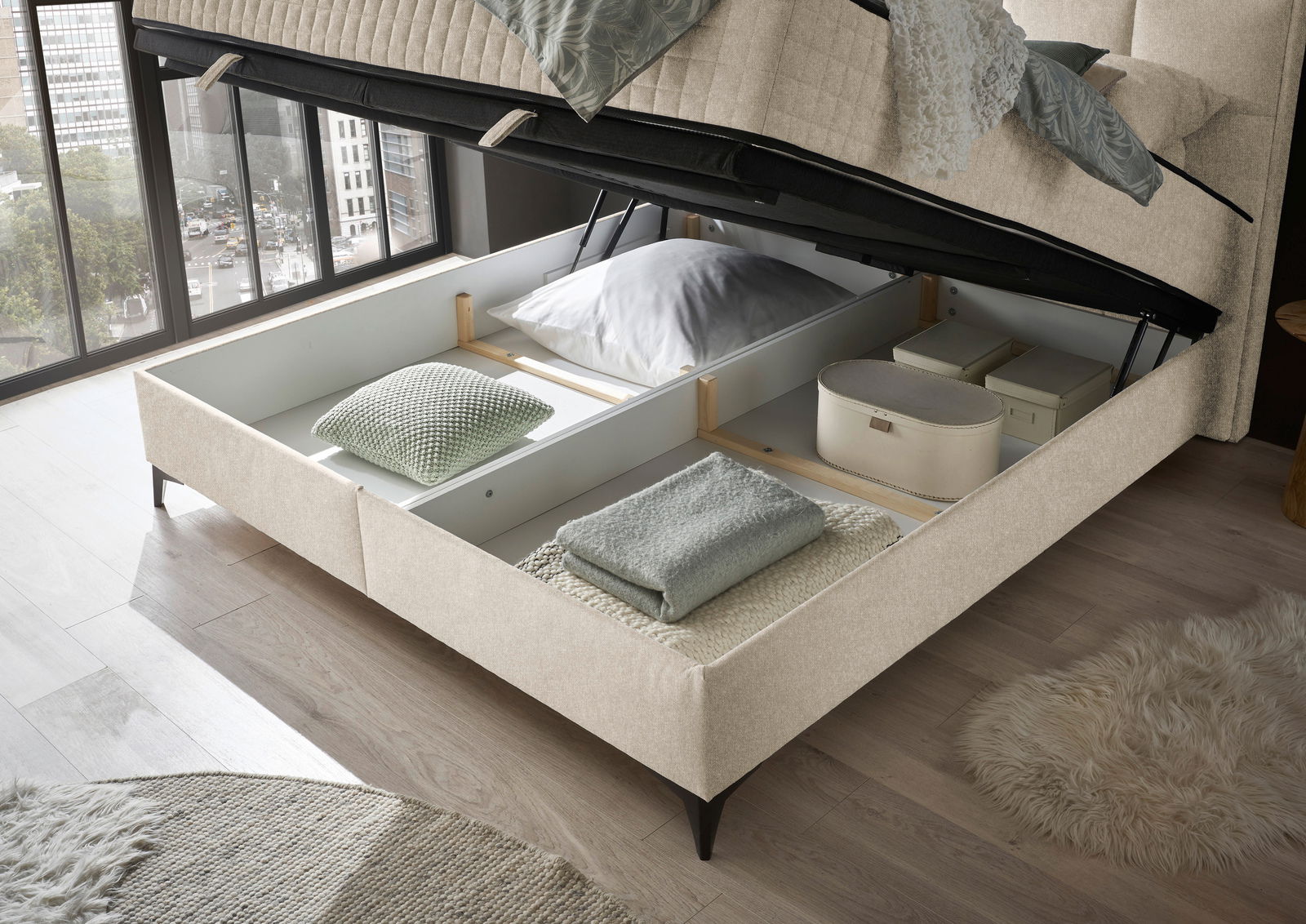 Boxbett mit geöffnetem Stauraum, von oben fotografiert, zeigt Kissen und Decken im Inneren.