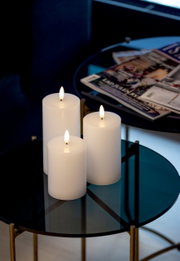 Drie witte, brandende led-kaarsen op een ronde glazen tafel, zijaanzicht