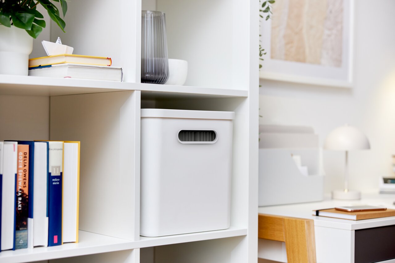 Weiße Archivbox in einem Regal, frontal fotografiert, umgeben von Büchern und Dekoration.